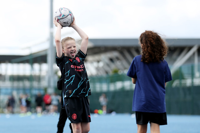 Two children playing soccer. One child is preparing to throw the ball while the other is waiting. One child is wearing a Manchester City jersey.
