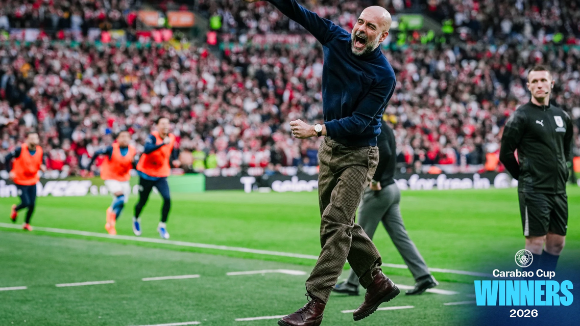A man in a blue sweater and brown pants is jumping in celebration on a football field. Behind him, players wearing orange vests are running. The background shows a stadium crowd. Text reads 'Carabao Cup Winners 2026'.