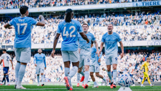 Manchester City players celebrating a goal at the Etihad Stadium during a match, with a crowd of spectators in the background.