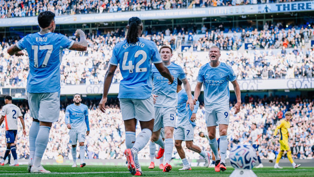 Manchester City players celebrating a goal at the Etihad Stadium during a match, with a crowd of spectators in the background.