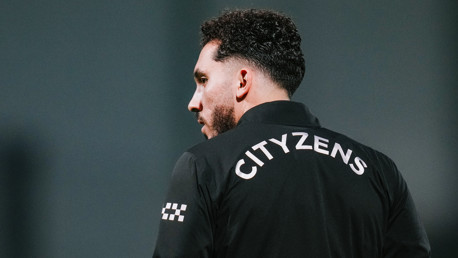 A person is turned away from the camera, wearing a jacket with 'CITYZENS' printed on the back. The face is blurred, and the background is plain.