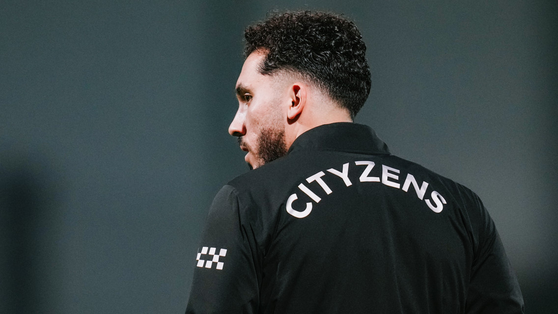 A person is turned away from the camera, wearing a jacket with 'CITYZENS' printed on the back. The face is blurred, and the background is plain.