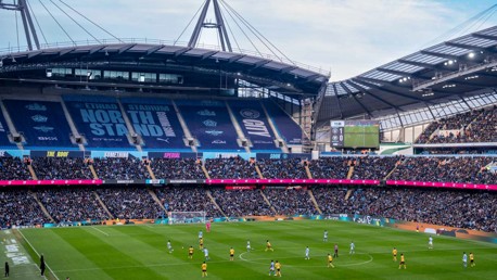 A football match taking place at Etihad Stadium, with a crowd and players on the pitch.