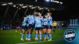 Women's soccer team with blurred faces celebrating on the field, wearing light blue jerseys with numbers and sponsor logos.