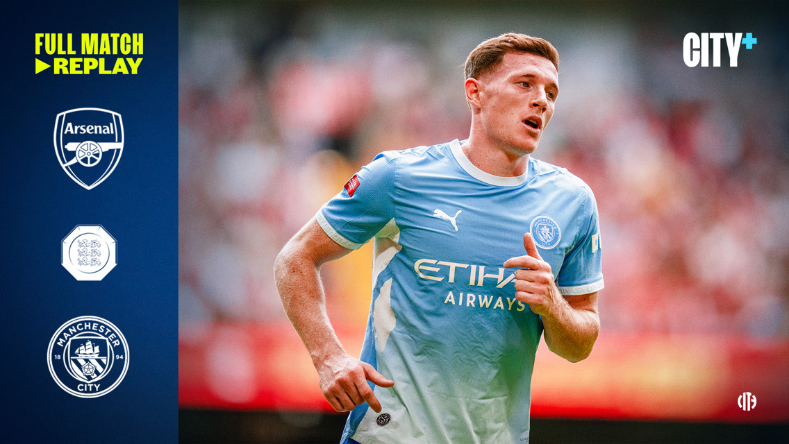 A Manchester City player in light blue kit during a match against Arsenal with logos and 'City+' branding on the sides.