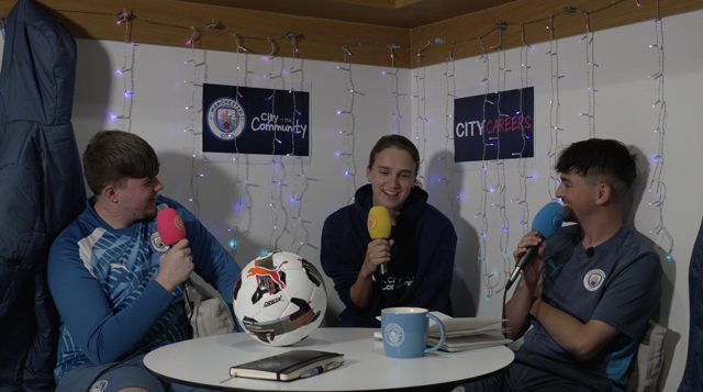 Three individuals participate in a podcast discussion, holding microphones with Manchester City branding. The setting includes Manchester City posters, fairy lights, and a football on the table.