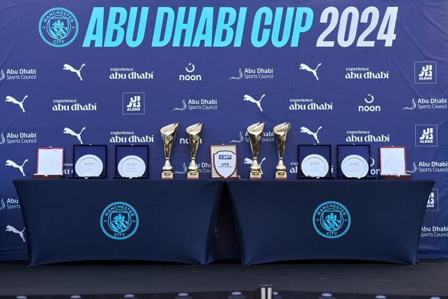 Trophies and awards displayed on tables with Manchester City branding at the Abu Dhabi Cup 2024 event.