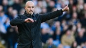 A man with a bald head wearing a black jacket gives a thumbs up gesture in a crowded setting.