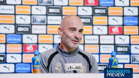 A person at a Manchester City press conference table with sponsorship logos in the background.