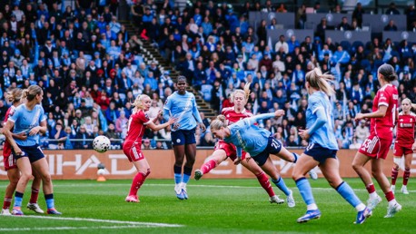 Women's soccer match with players in blue and red jerseys in action on the field, surrounded by a crowd of spectators.
