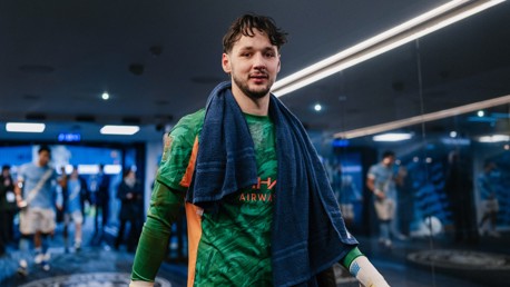 A football player wearing green Manchester City kit walks in a tunnel, holding a towel draped around his neck.