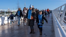 A group of people walking on a bridge wearing Manchester City scarves, suggesting they are fans attending a football match.