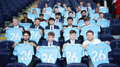 A group of young individuals in suits holding Manchester City jerseys with 'Class of 26' written on them, seated in a stadium.