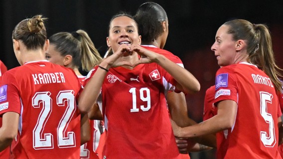 Swiss women's soccer team celebrating a goal. The player wearing jersey number 19 forms a heart shape with her hands.