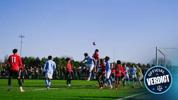 Youth soccer match with players in red and blue jerseys competing near the goal, with a soccer ball in the air and an official badge overlay.