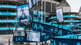 An outdoor exhibit at Etihad Stadium featuring portraits and signage related to Manchester City with stadium architecture in the background.