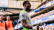 A football player wearing a Manchester City jersey celebrates during a match, showing the Premier League logo and 'No room for racism' on the sleeve.