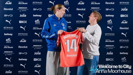 Two individuals are holding a Manchester City shirt with the name 'Moorhouse' and the number '14'. The background includes various sponsor logos. Text reads 'Welcome to City Anna Moorhouse'.