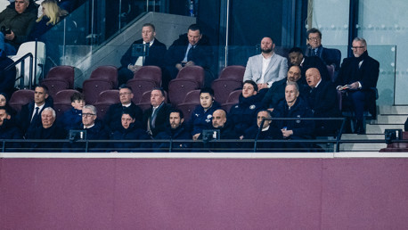 A group of people seated in a VIP area of a stadium, watching an event.