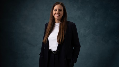A woman wearing a black suit and white shirt against a dark blue background. Her face is blurred for privacy.