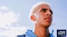 Close-up of a person wearing a light blue jacket against a bright sky. The image features the text 'Asia Tour '26' presented by Experience Abu Dhabi.
