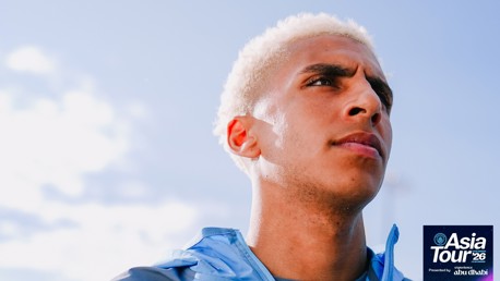 Close-up of a person wearing a light blue jacket against a bright sky. The image features the text 'Asia Tour '26' presented by Experience Abu Dhabi.