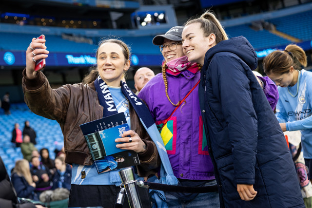 Three fans taking a selfie at Etihad Stadium, wearing Manchester City merchandise.