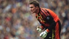A football goalkeeper wearing a brightly colored uniform and gloves is ready for action in a stadium.