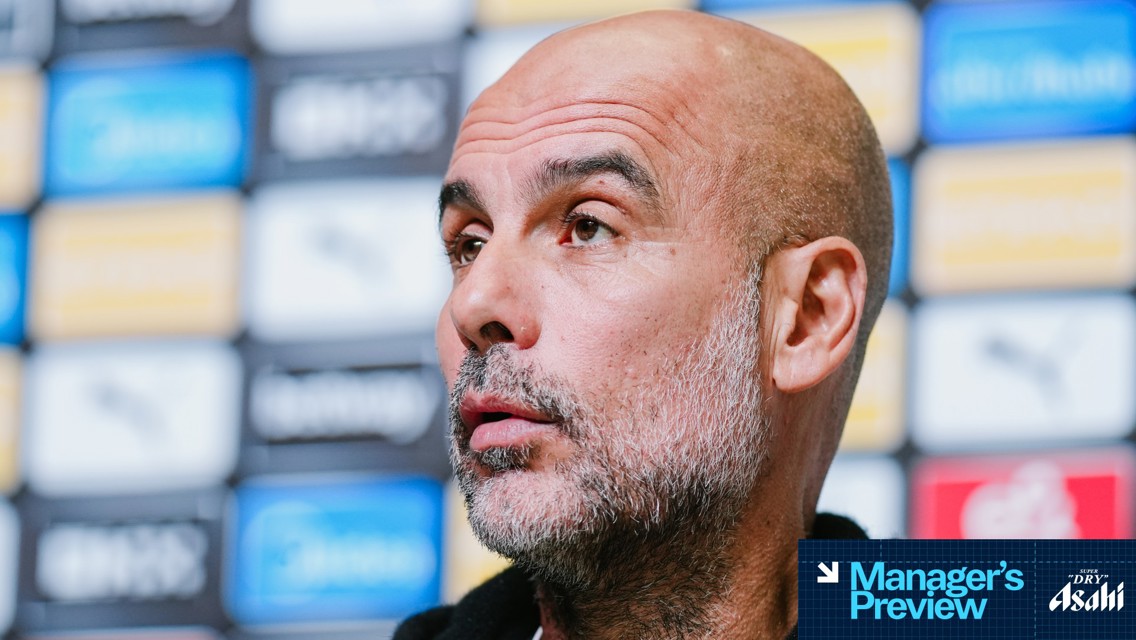 Blurred image showing the presumed bald head of a person possibly Pep Guardiola due to the setting of a football press conference with logos in the background, hinting at a Manchester City context.