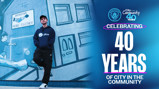 A person in a Man City Community hoodie stands in front of a mural with 'Bringing People Together' accompanied by text celebrating 40 years of 'City in the Community' with Manchester City logos.
