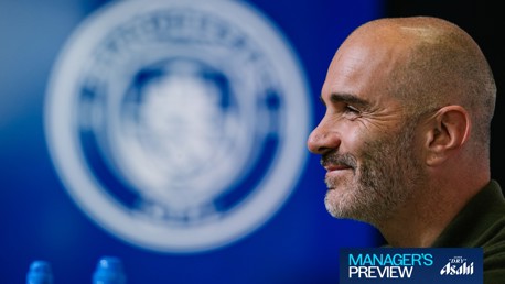 A person with a shaved head and beard is smiling in profile view. The background features a blurred circular logo. Text in the bottom corner reads 'MANAGER'S PREVIEW' and 'Super Dry Asahi'.