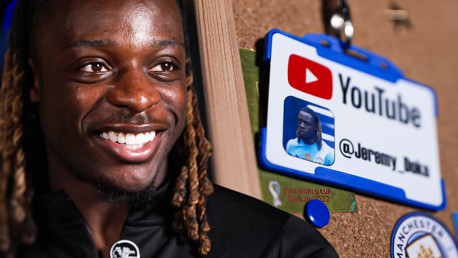 A close-up of a YouTube badge with the handle @Jeremy_Doku, hanging on a pinboard next to a FIFA World Cup Qatar 2022 sticker and a Manchester City logo.