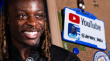 A close-up of a YouTube badge with the handle @Jeremy_Doku, hanging on a pinboard next to a FIFA World Cup Qatar 2022 sticker and a Manchester City logo.