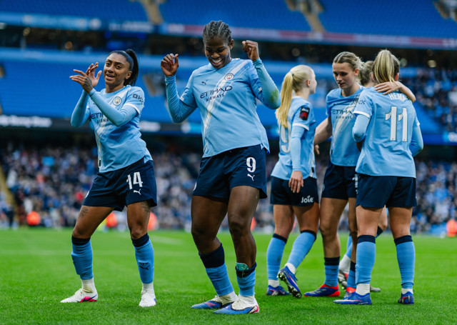 Group of Manchester City women players celebrating on the field wearing light blue jerseys with numbers visible.