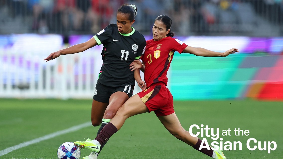 Two soccer players from opposing teams compete for control of the ball during a match. The text 'City at the Asian Cup' is visible on the image.