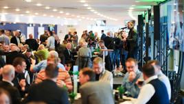 A business conference with attendees seated at tables. A musician performs on stage with a guitar and microphone.