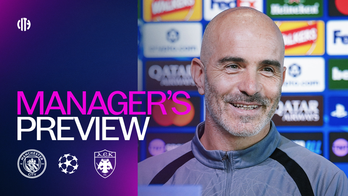 Image of a manager's preview for a Manchester City vs AEK Athens UEFA Champions League match, with a smiling coach in front of sponsor boards.