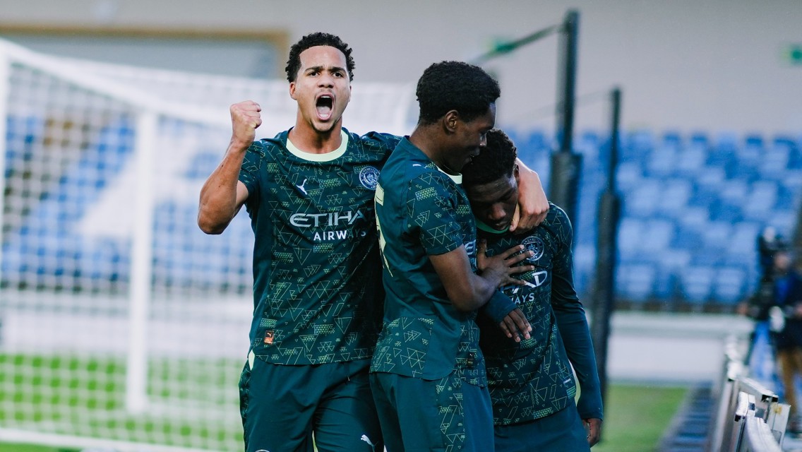 Football players in Manchester City kit celebrating a goal on the field with blurred faces