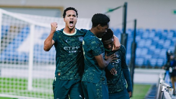 Football players in Manchester City kit celebrating a goal on the field with blurred faces