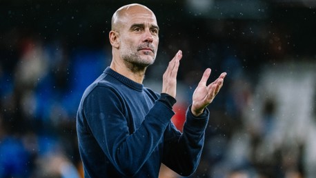An individual in a dark sweater claps hands in a soccer stadium, with blurred face, suggesting likely context of supporting team or a match.