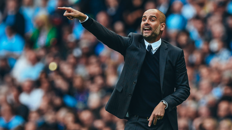 A man in a suit, possibly a coach, is pointing with his arm extended in front of an audience.