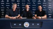 Three individuals seated at a table with Manchester City branding, featuring a contract and pen.