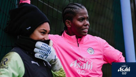Two individuals at a sports training session wearing Manchester City gear; one in a pink tracksuit.