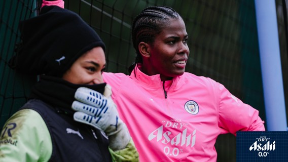 Two individuals at a sports training session wearing Manchester City gear; one in a pink tracksuit.