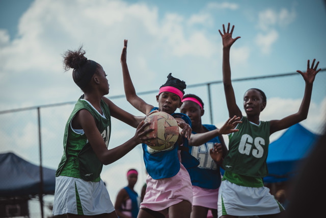Group of players in netball game, wearing colorful uniforms, holding and defending the ball.