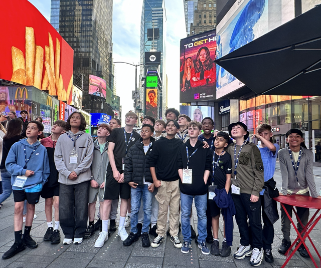 A group of people with lanyards and name tags, standing in Times Square, New York City, surrounded by billboards and advertisements.