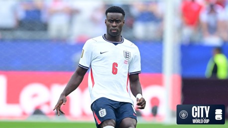 A soccer player wearing an England jersey with number 6 participates in a game. The background includes blurred crowd and event signage. 'City at the World Cup' is visible at the bottom right.