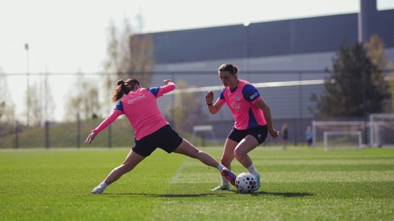 Two soccer players in pink bibs practicing on a field, one attempting a tackle.
