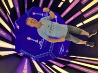 A person wearing an Etihad Airways jersey and shorts stands in front of displays related to the FIFA Club World Cup Saudi Arabia 2023, surrounded by purple #ClubWC and trophy-themed lighting elements.