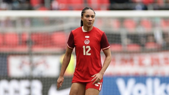 A soccer player wearing a red Canada jersey with the number 12 is standing on the field during a match.